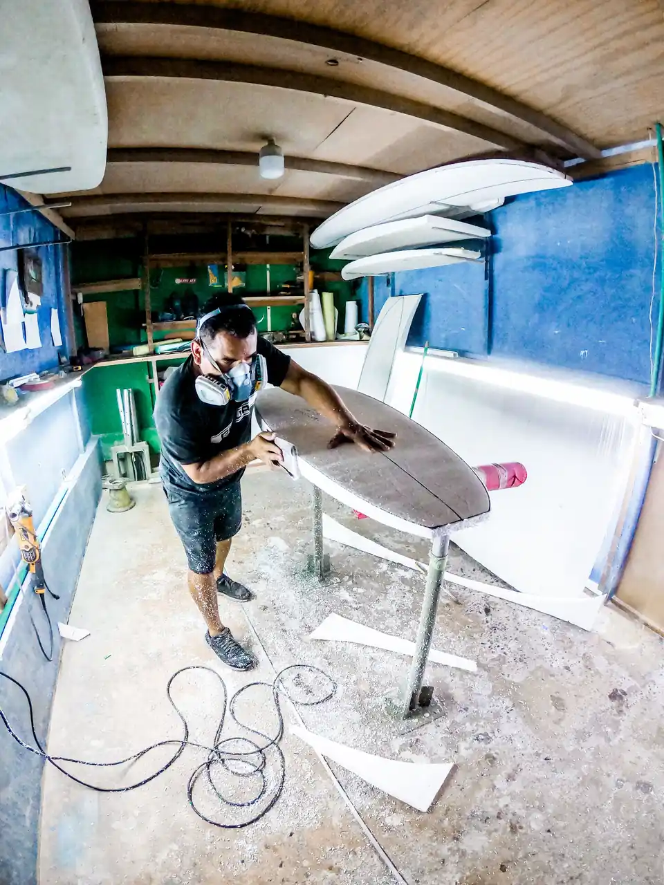 A craftsman in a respirator sanding a surfboard in a workshop